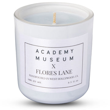 White candle with 'Academy Museum x Flores Lane' label on a white  Indulge in the LOW RESOLUTION CANDLE, an 8oz soy candle featuring leather and smoked cognac scents. 40 hours of eco-friendly luxury in a recycled glass vessel.background FLORES LANE MOVIE GENRE SCENTED CANDLE: FILM NOIR | ACADEMY MUSEUM